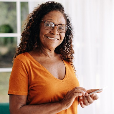 Senior woman with glasses smiling while looking at phone