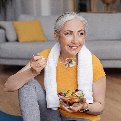 Senior woman smiling while eating salad at home