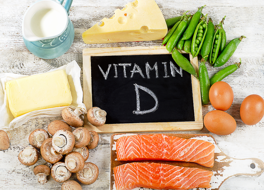 A chalk board with "vitamin D" written on it surrounded by foods like cheese, milk, eggs, veggies, salmon